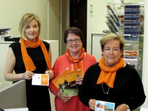 Kolme naista oransseilla huiveilla esittää erilaisia postikortteja.