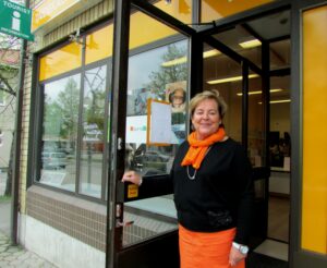 Oranssiin ja mustaan pukeutunut vaaleahiuksinen nainen avaa oven infon uuteen tilaan.